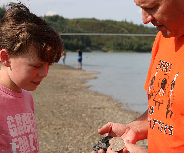 Boy holds a bucket of rocks and stands in shallow river water.