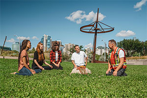 Keith Diakiw, P.Geo., Talking Rock Tours sits with tour attendees in a field on a sunny summer day.